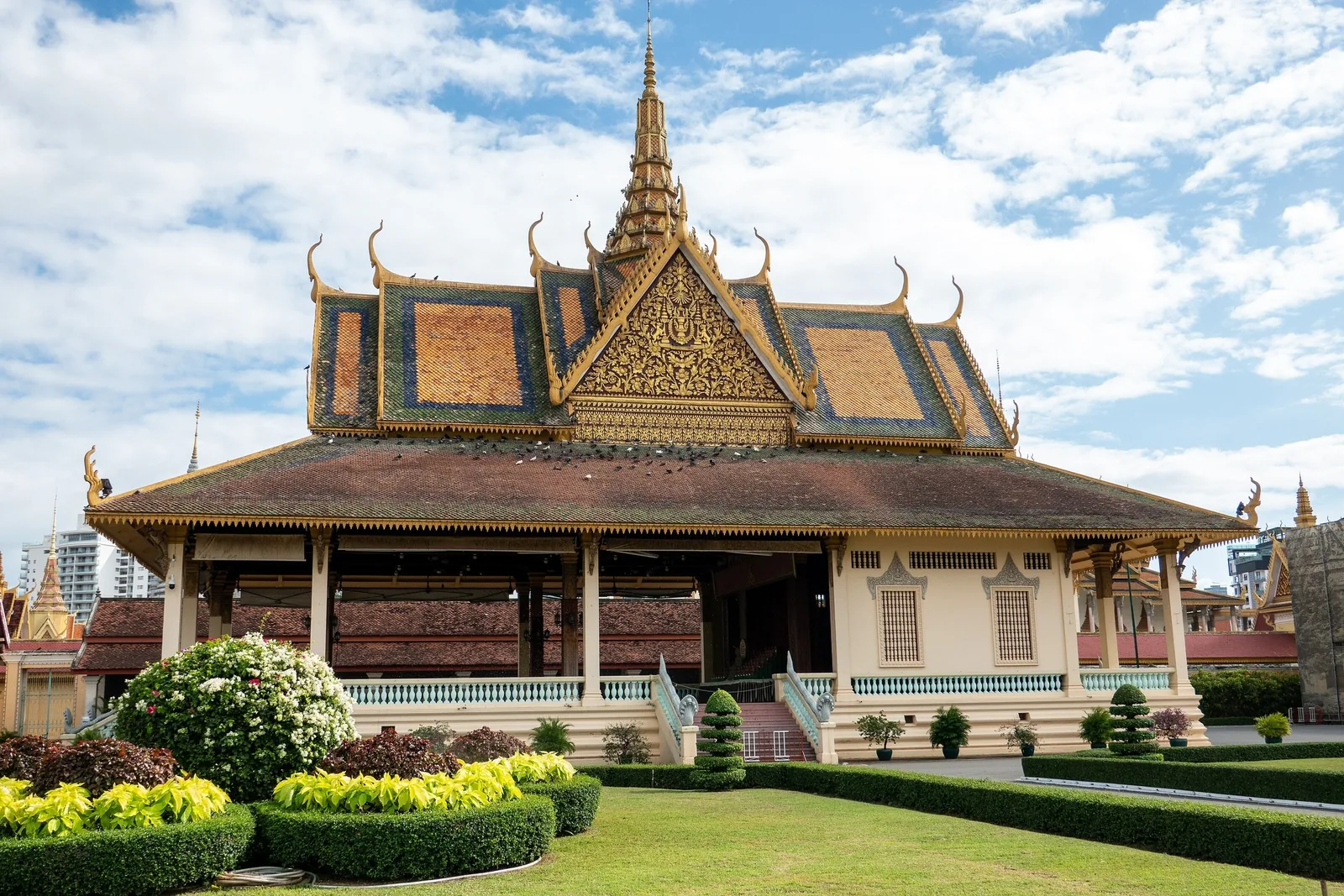 Ornate spired pavilion with golden roof tiles at the Royal Palace complex in Phnom Penh, set behind manicured gardens.