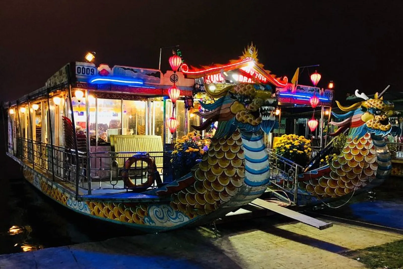 A colorful dragon-shaped boat lit with lanterns and neon at night on the Perfume River in Hue.